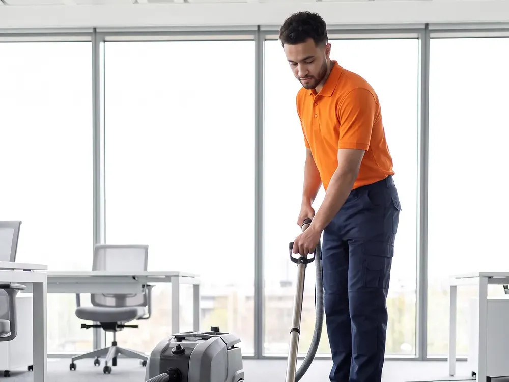 Agent d'entretien en polo orange nettoyant la moquette d'un open space à l'injecteur-extracteur : la bande nettoyée se voit derrière la buse