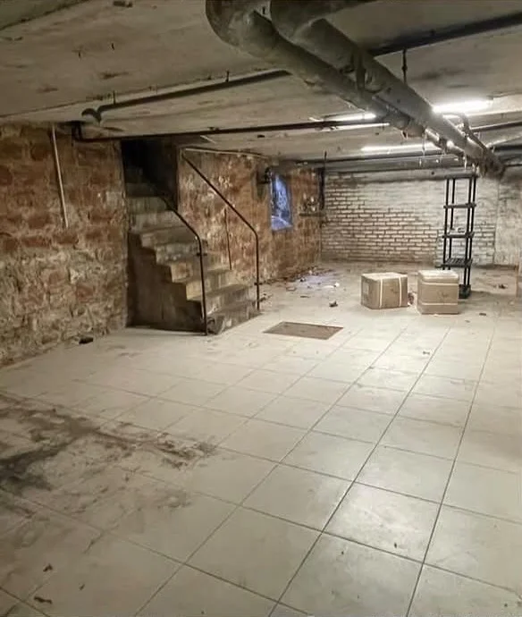 Grande cave avant le nettoyage, sol taché et cartons au milieu de la pièce